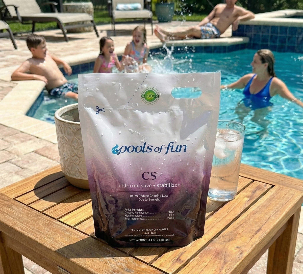 Bag of 'Pools of Fun' pool chemical on a table with people in the background by a pool.