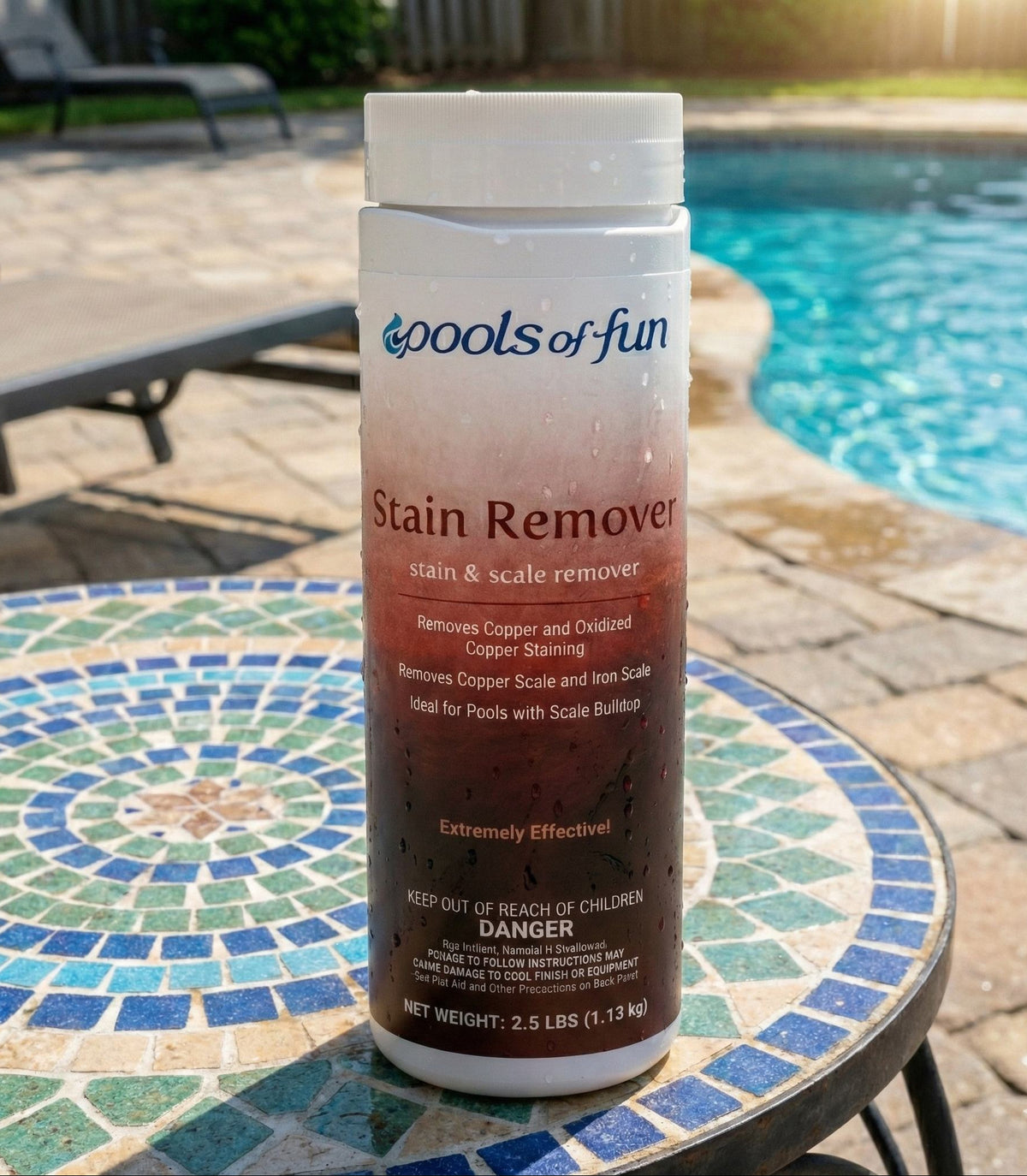 Pump bottle of 'Pools of Fun' Stain Remover on a mosaic table by a pool.