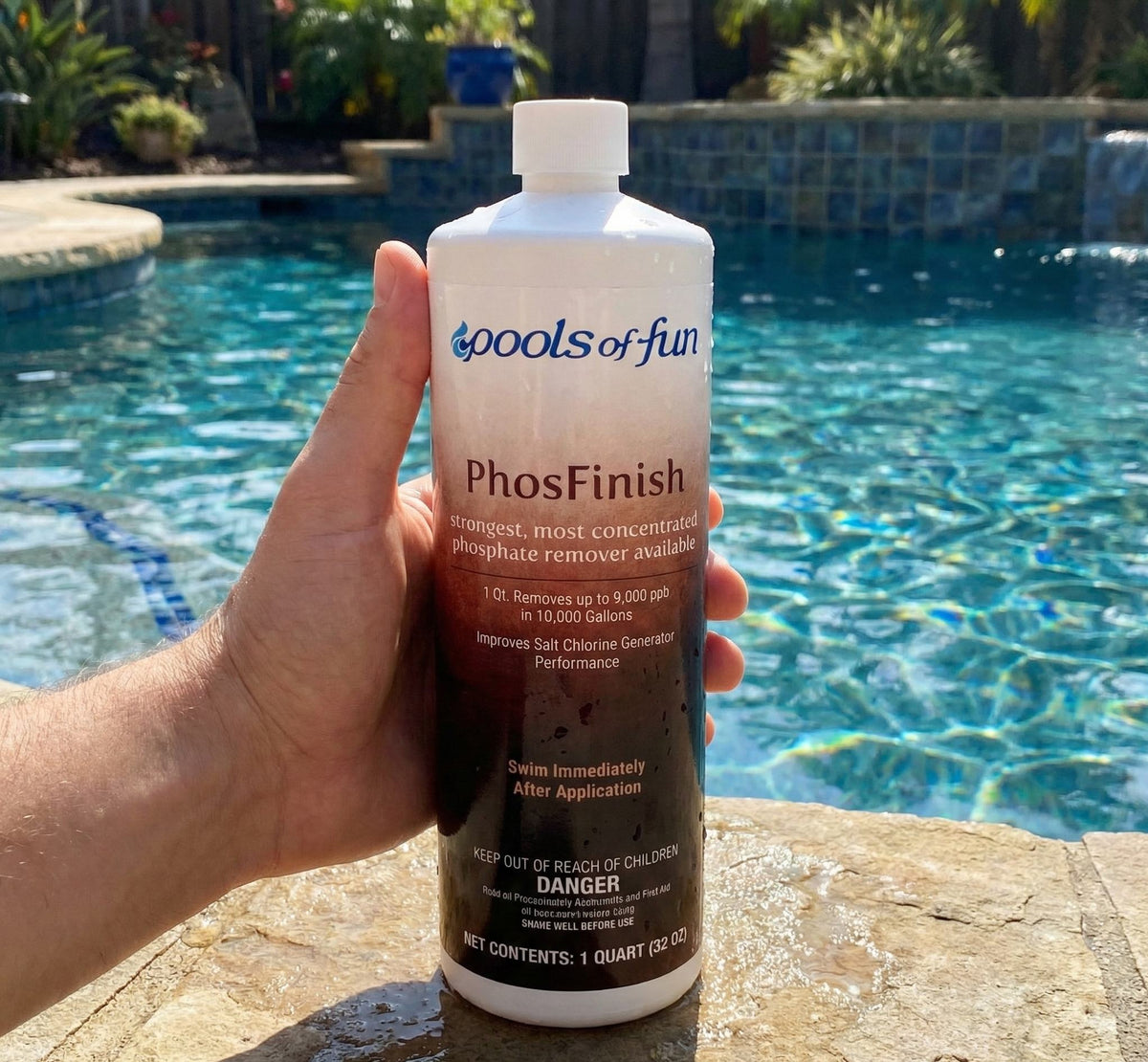 Person holding a bottle of 'Pools of Fun PhosFinish' by a pool.